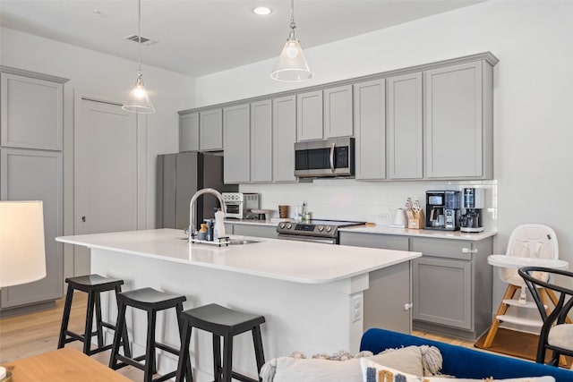 kitchen with appliances with stainless steel finishes, an island with sink, light hardwood / wood-style flooring, and gray cabinets