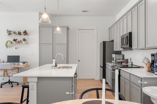 kitchen with appliances with stainless steel finishes, gray cabinetry, light hardwood / wood-style floors, and sink