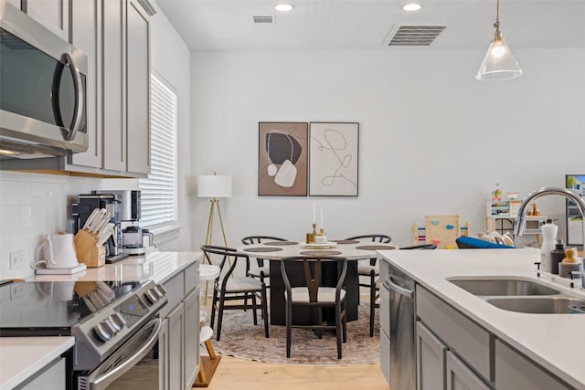 kitchen featuring gray cabinets, light wood-type flooring, sink, stainless steel appliances, and decorative light fixtures