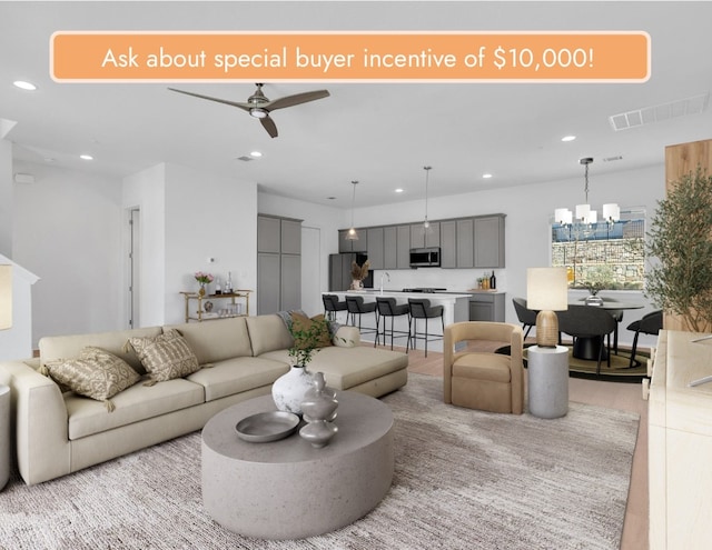 living room featuring light wood-style floors, ceiling fan with notable chandelier, visible vents, and recessed lighting