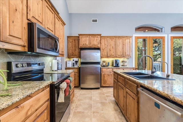 kitchen with appliances with stainless steel finishes, light stone countertops, sink, and light tile patterned floors