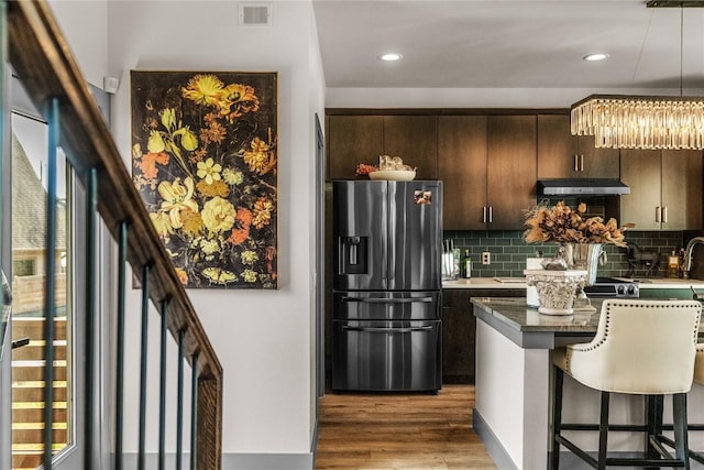 kitchen featuring decorative backsplash, dark brown cabinets, hardwood / wood-style flooring, stainless steel fridge with ice dispenser, and a center island