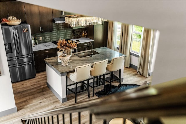 kitchen with decorative backsplash, stainless steel refrigerator with ice dispenser, dark brown cabinets, sink, and light hardwood / wood-style flooring