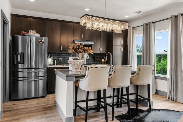 kitchen featuring stainless steel fridge, dark brown cabinetry, a center island with sink, and light hardwood / wood-style floors