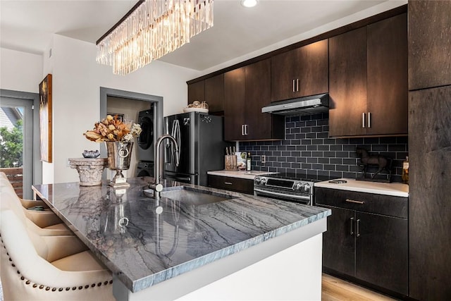 kitchen featuring light hardwood / wood-style flooring, dark stone counters, a kitchen island with sink, stacked washer and clothes dryer, and appliances with stainless steel finishes