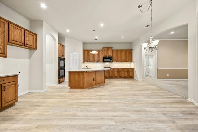 kitchen with an inviting chandelier, black appliances, a center island with sink, and decorative light fixtures