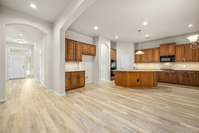 kitchen featuring hanging light fixtures, a center island with sink, black appliances, light hardwood / wood-style floors, and decorative backsplash