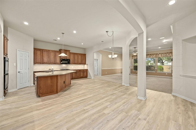 kitchen featuring an island with sink, black appliances, light hardwood / wood-style flooring, and decorative light fixtures