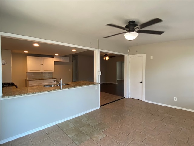 kitchen featuring white cabinets, kitchen peninsula, light stone countertops, ceiling fan, and sink