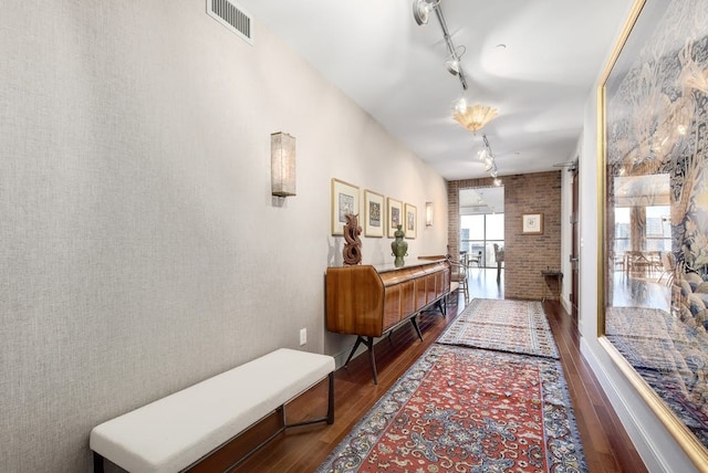 corridor featuring brick wall, track lighting, and hardwood / wood-style flooring