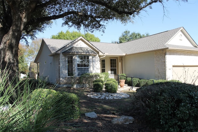 ranch-style home featuring a garage, stone siding, a shingled roof, and stucco siding