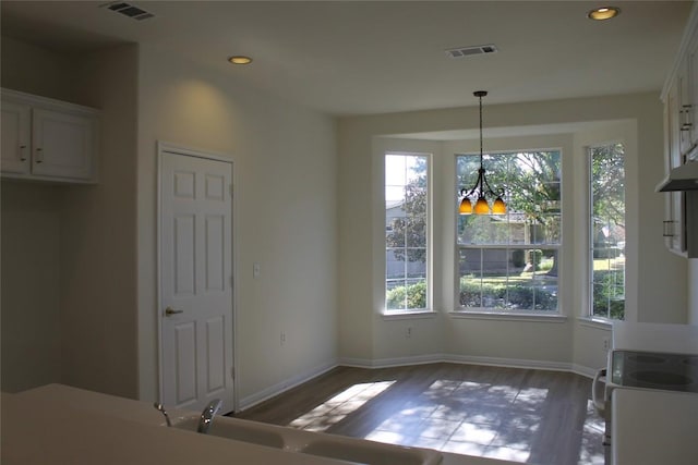 unfurnished dining area featuring baseboards, visible vents, wood finished floors, an inviting chandelier, and recessed lighting