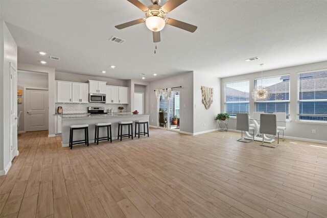 living room featuring ceiling fan with notable chandelier and light wood-type flooring