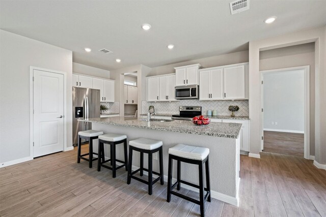 kitchen featuring a kitchen breakfast bar, light stone counters, a center island with sink, white cabinets, and appliances with stainless steel finishes