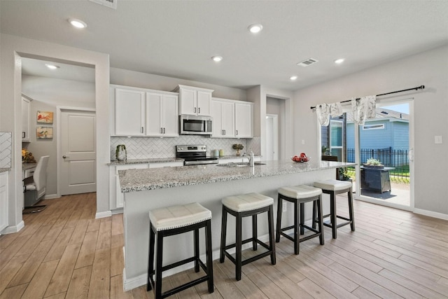 kitchen with appliances with stainless steel finishes, white cabinetry, light stone counters, and a kitchen island with sink