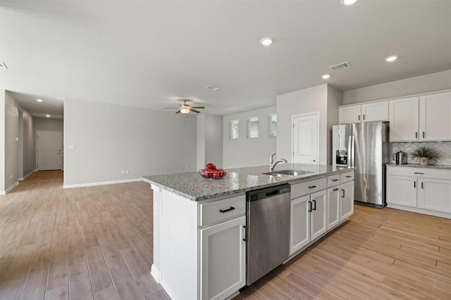 kitchen with light stone countertops, white cabinetry, a center island with sink, and stainless steel appliances