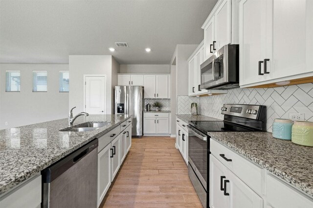 kitchen featuring white cabinets, sink, light wood-type flooring, light stone countertops, and appliances with stainless steel finishes