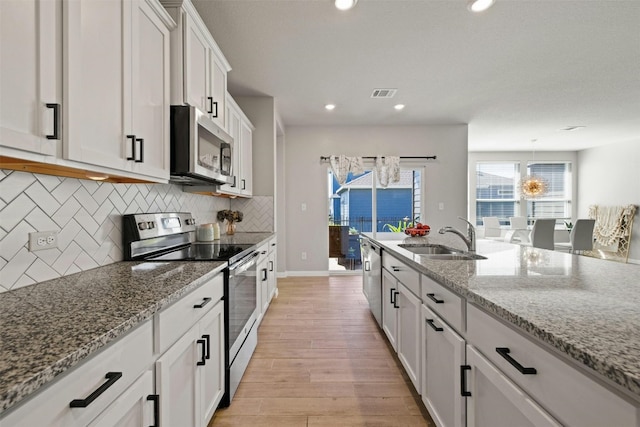 kitchen with white cabinetry, sink, light stone countertops, light hardwood / wood-style flooring, and appliances with stainless steel finishes