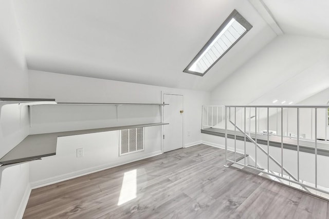 additional living space with lofted ceiling with skylight, visible vents, and wood finished floors