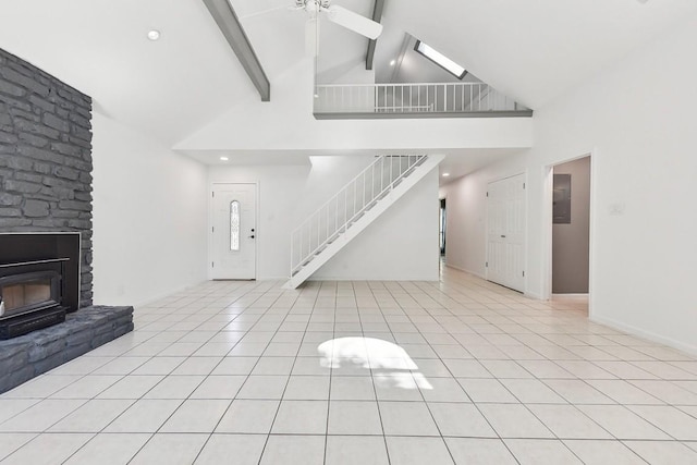 unfurnished living room with a wood stove, ceiling fan, beamed ceiling, high vaulted ceiling, and light tile patterned flooring