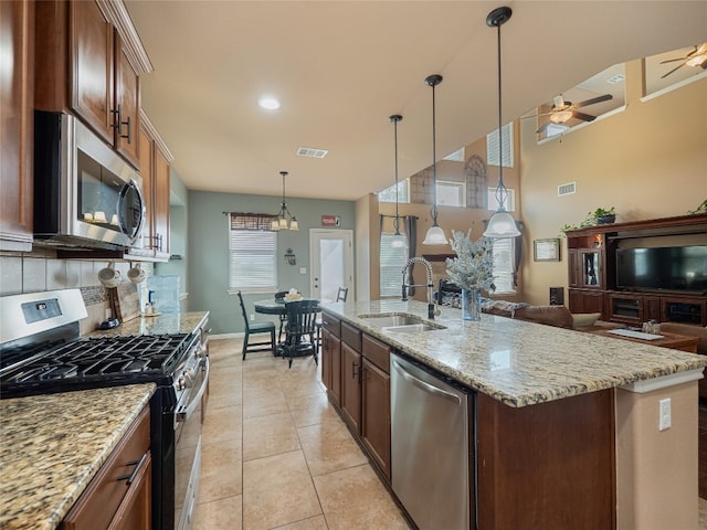 kitchen with an island with sink, sink, tasteful backsplash, decorative light fixtures, and appliances with stainless steel finishes