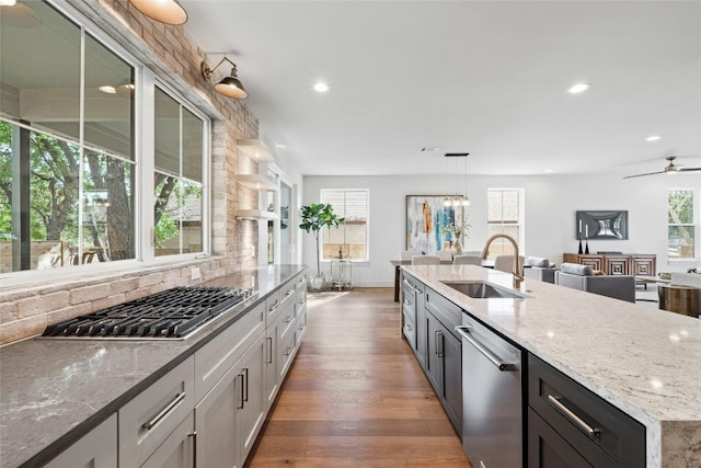 kitchen with hanging light fixtures, sink, dark wood-type flooring, light stone counters, and stainless steel appliances