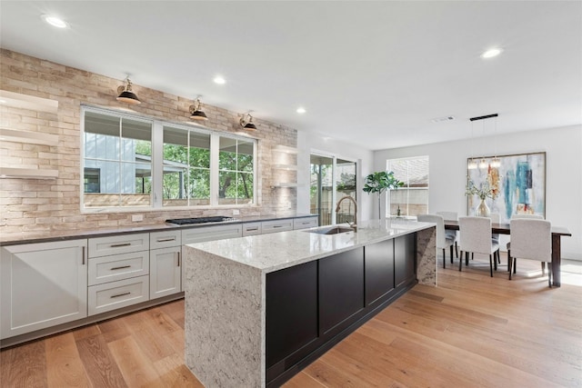 kitchen featuring pendant lighting, sink, light stone countertops, an island with sink, and light hardwood / wood-style floors