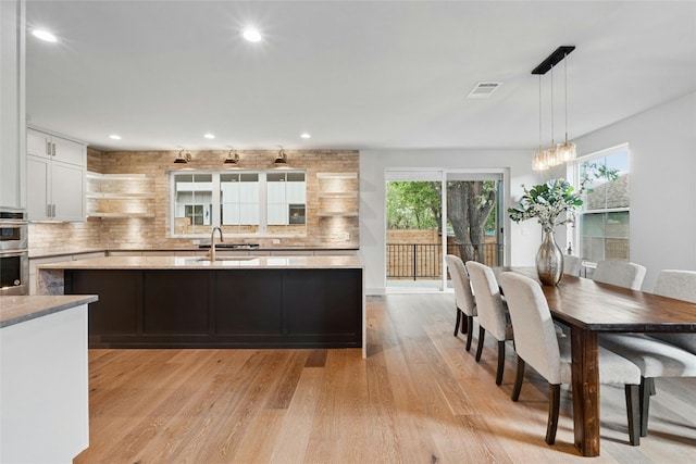 kitchen with pendant lighting, stainless steel double oven, white cabinetry, tasteful backsplash, and light wood-type flooring