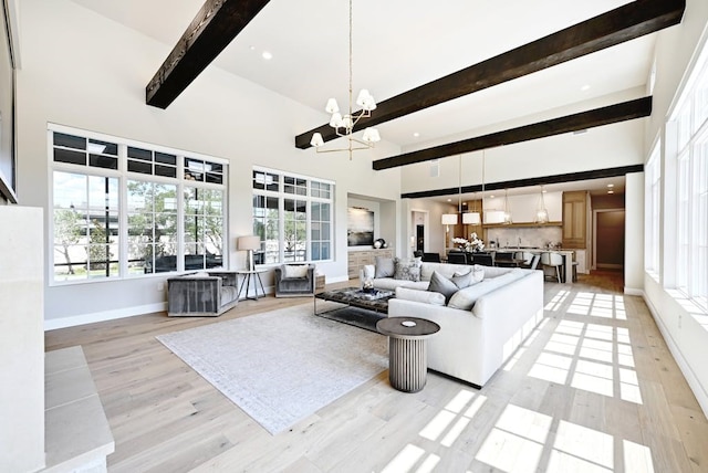 living room with beam ceiling, a high ceiling, a chandelier, and light hardwood / wood-style flooring