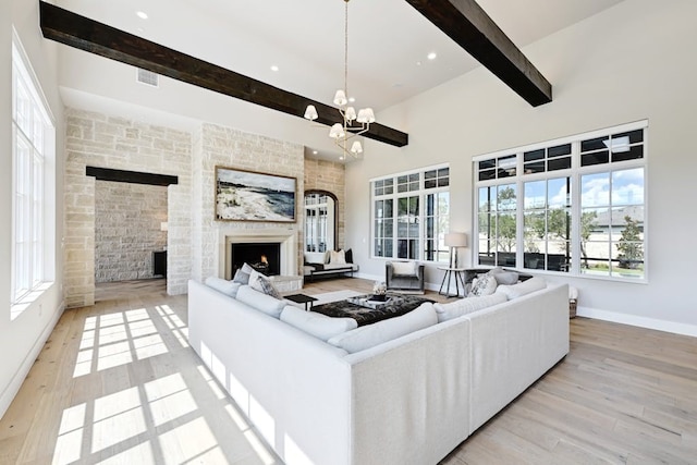 living room featuring a towering ceiling, a notable chandelier, a fireplace, light hardwood / wood-style floors, and beamed ceiling