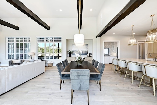 dining area featuring beamed ceiling, light hardwood / wood-style floors, sink, and a high ceiling