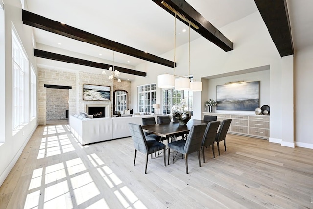 dining area featuring light hardwood / wood-style flooring, a towering ceiling, a fireplace, and beamed ceiling