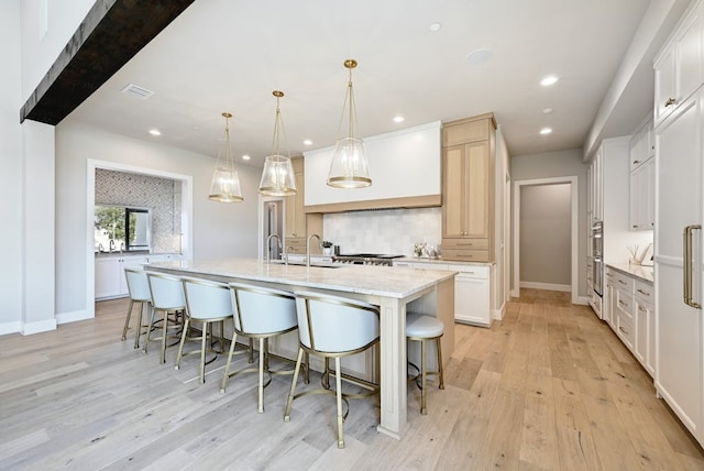 kitchen featuring hanging light fixtures, a center island with sink, white cabinets, and decorative backsplash