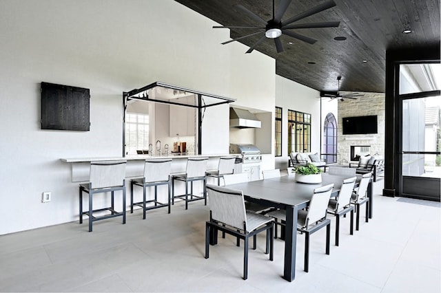 dining area featuring sink, a stone fireplace, ceiling fan, and a high ceiling