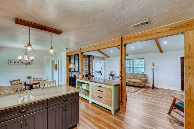 kitchen featuring hanging light fixtures, light stone countertops, light wood-type flooring, vaulted ceiling with beams, and a notable chandelier