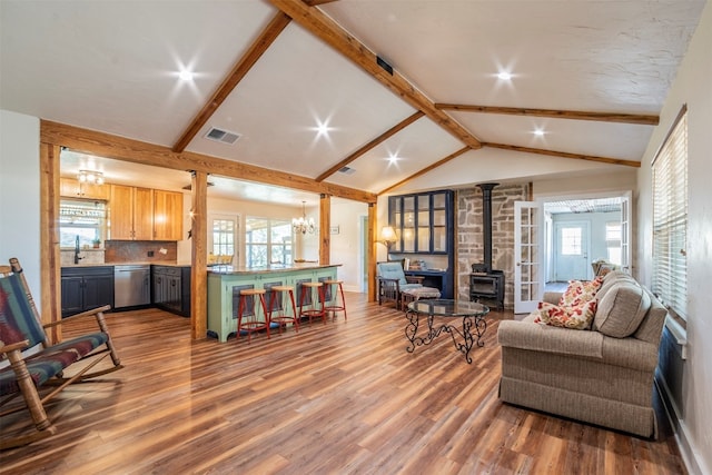 living room with a healthy amount of sunlight, lofted ceiling with beams, a wood stove, and hardwood / wood-style flooring