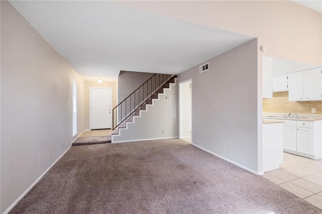 unfurnished living room featuring sink, light colored carpet, and a textured ceiling