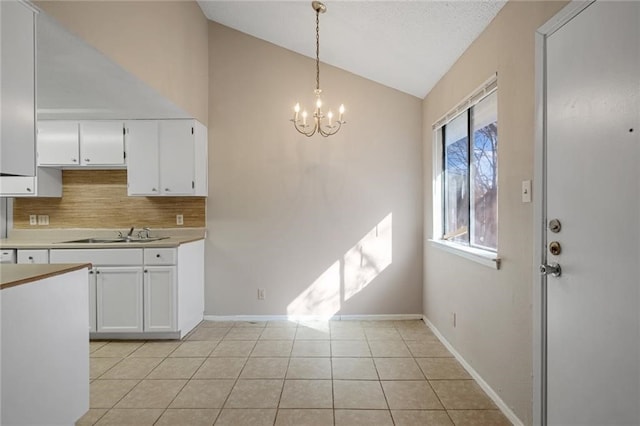 kitchen with white cabinetry, sink, lofted ceiling, and hanging light fixtures