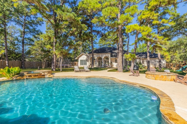 view of pool featuring a trampoline, a patio area, a fenced backyard, and an outdoor fire pit