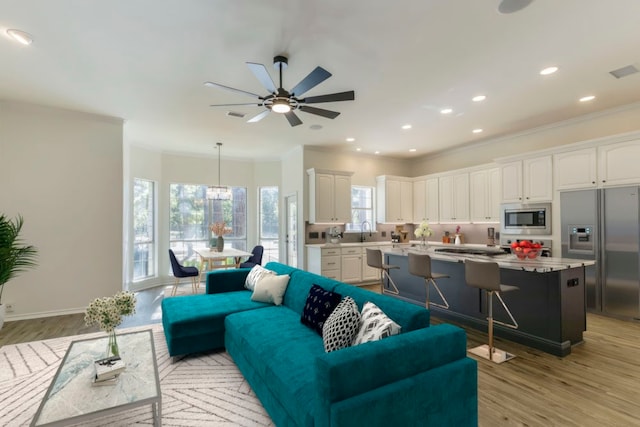 living room with ceiling fan with notable chandelier, sink, light hardwood / wood-style flooring, and ornamental molding