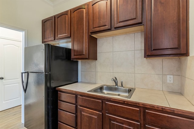 kitchen featuring crown molding, tile counters, decorative backsplash, freestanding refrigerator, and a sink