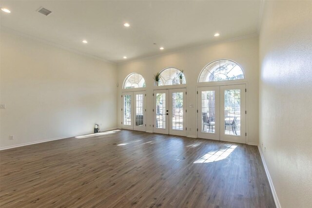 empty room with french doors, crown molding, dark wood-type flooring, and a healthy amount of sunlight