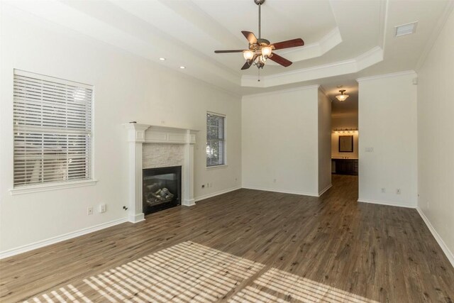 unfurnished living room with ceiling fan, a tray ceiling, dark hardwood / wood-style floors, and crown molding