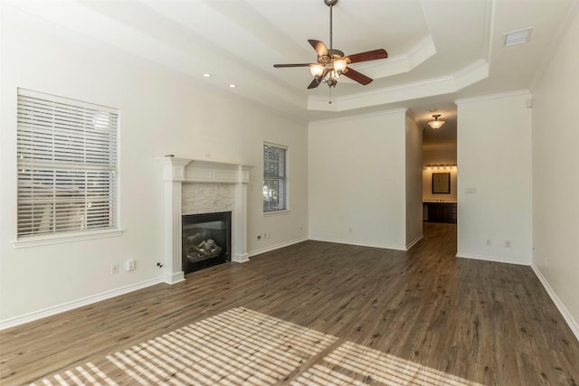 unfurnished living room with ornamental molding, a ceiling fan, a tray ceiling, a glass covered fireplace, and wood finished floors