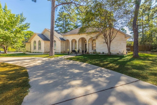 view of front of home featuring stone siding, driveway, a front yard, and fence