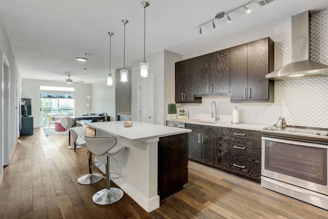 kitchen featuring hardwood / wood-style flooring, electric range, sink, wall chimney exhaust hood, and decorative backsplash