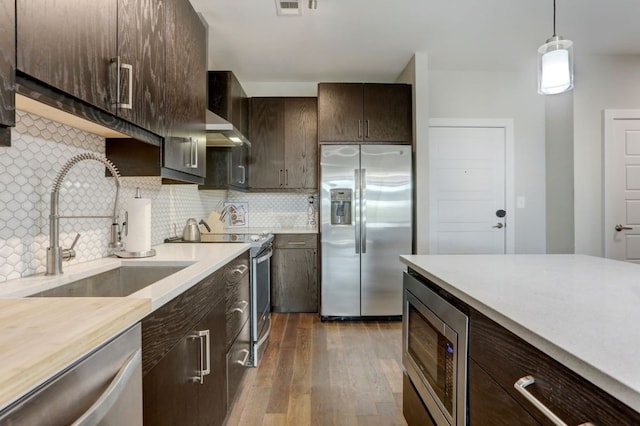 kitchen featuring dark brown cabinets, hanging light fixtures, stainless steel appliances, backsplash, and dark hardwood / wood-style flooring