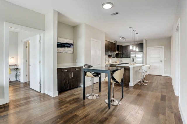 kitchen featuring a kitchen breakfast bar, a kitchen island, dark brown cabinets, dark hardwood / wood-style floors, and stainless steel fridge with ice dispenser