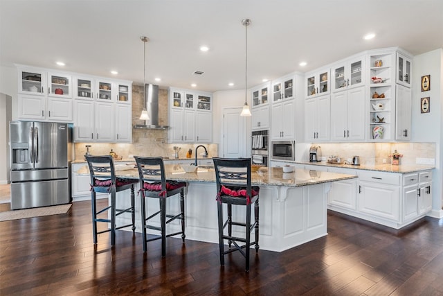 kitchen featuring white cabinets, appliances with stainless steel finishes, a large island with sink, and wall chimney range hood