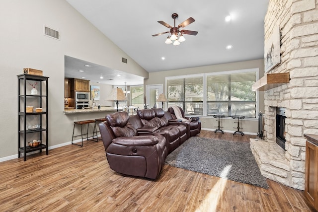 living room featuring high vaulted ceiling, ceiling fan, light hardwood / wood-style floors, and a fireplace